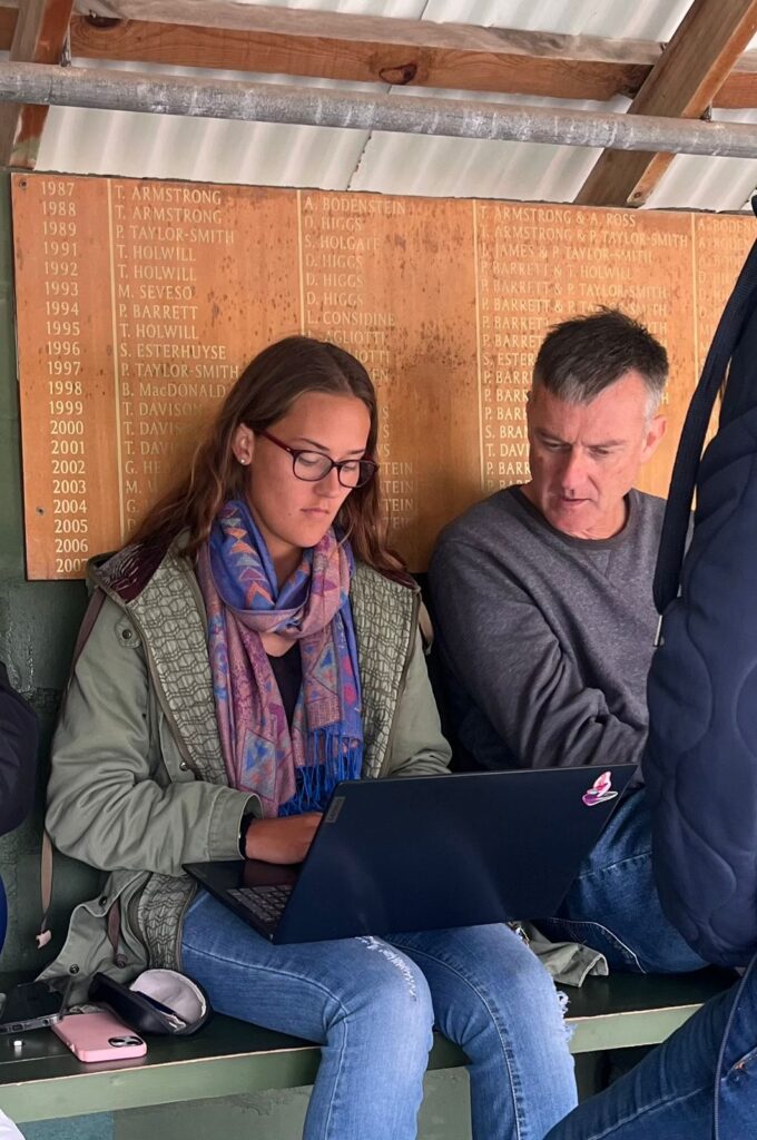 Fish Hoek Tennis Club Championship organizers sit on bench while looking at laptop screen and organizing club champs matches.